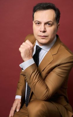 Man in brown suit posing against maroon backdrop